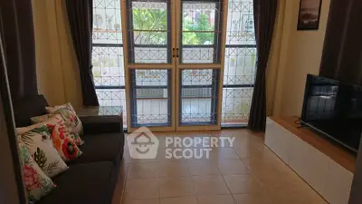 Cozy living room with tiled floor, sofa, TV, and garden view through large windows.
