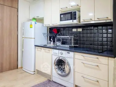 Modern kitchen with washing machine, microwave, and fridge in sleek apartment.