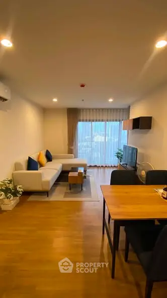 Modern living room with cozy sofa and dining area, featuring wooden flooring and large window.