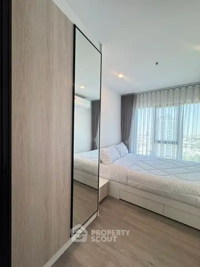 Modern bedroom with large window and mirrored wardrobe in a high-rise apartment.