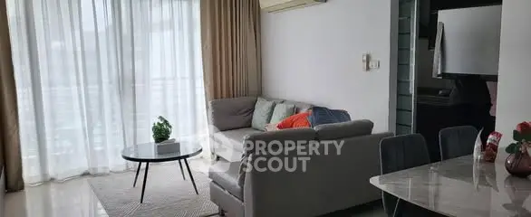 Modern living room with cozy sofa and dining area, featuring large windows and natural light.
