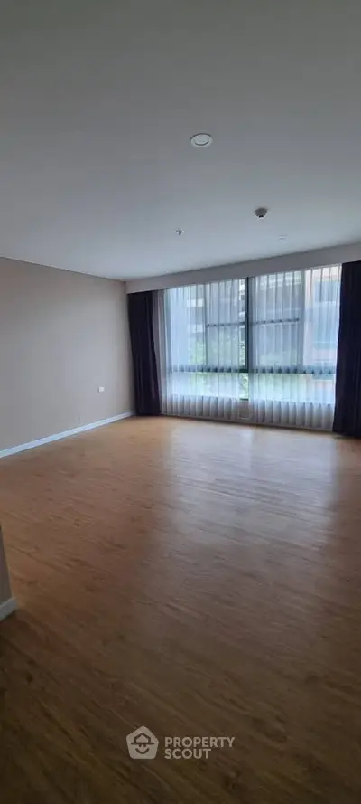 Spacious empty living room with large windows and wooden flooring, perfect for customization.