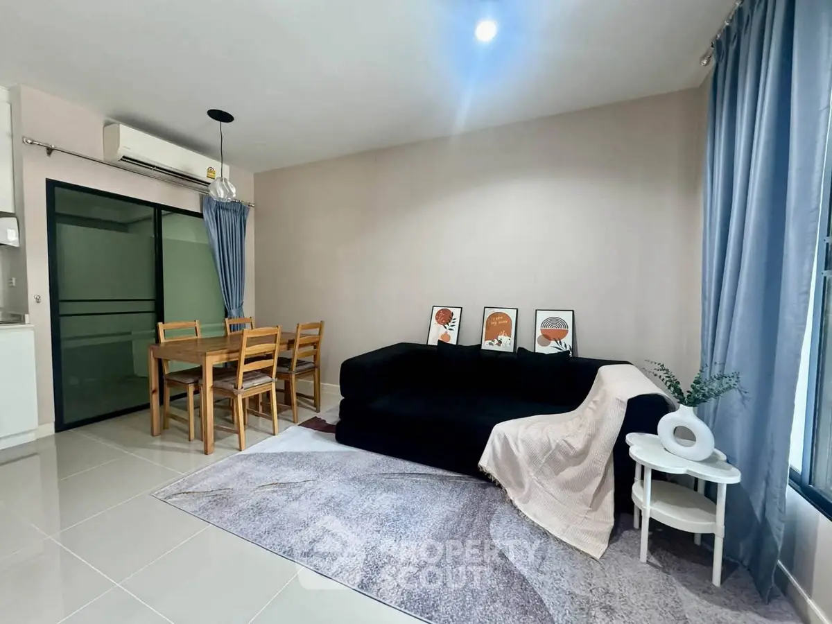 Modern living room with sleek black sofa, dining area, and stylish decor in a cozy apartment.