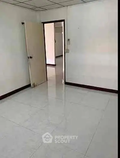 Spacious empty room with tiled flooring and open door, ideal for customization.