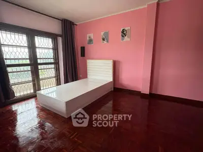 Spacious bedroom with pink walls, large window, and wooden flooring, perfect for a cozy retreat.