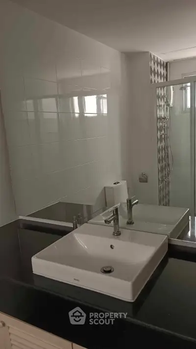 Modern bathroom with sleek sink and glass shower enclosure, featuring stylish tile accents.