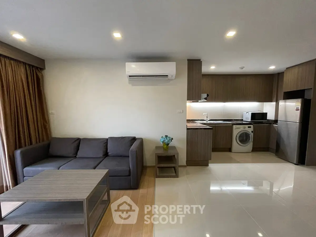 Modern living room with open kitchen, featuring a cozy sofa and washing machine.