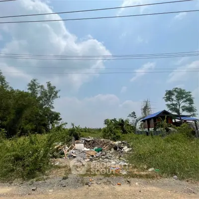 Vacant land with debris and a small structure under a clear sky, ideal for development.