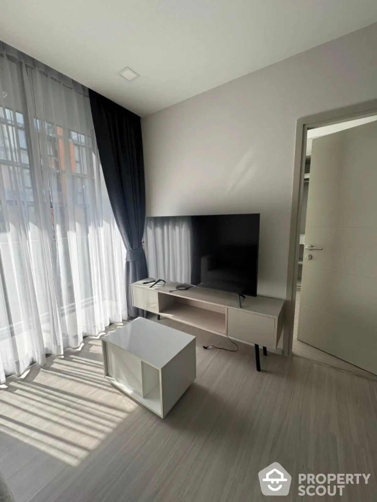 Modern living room with large TV and stylish furniture, featuring floor-to-ceiling windows and elegant curtains.