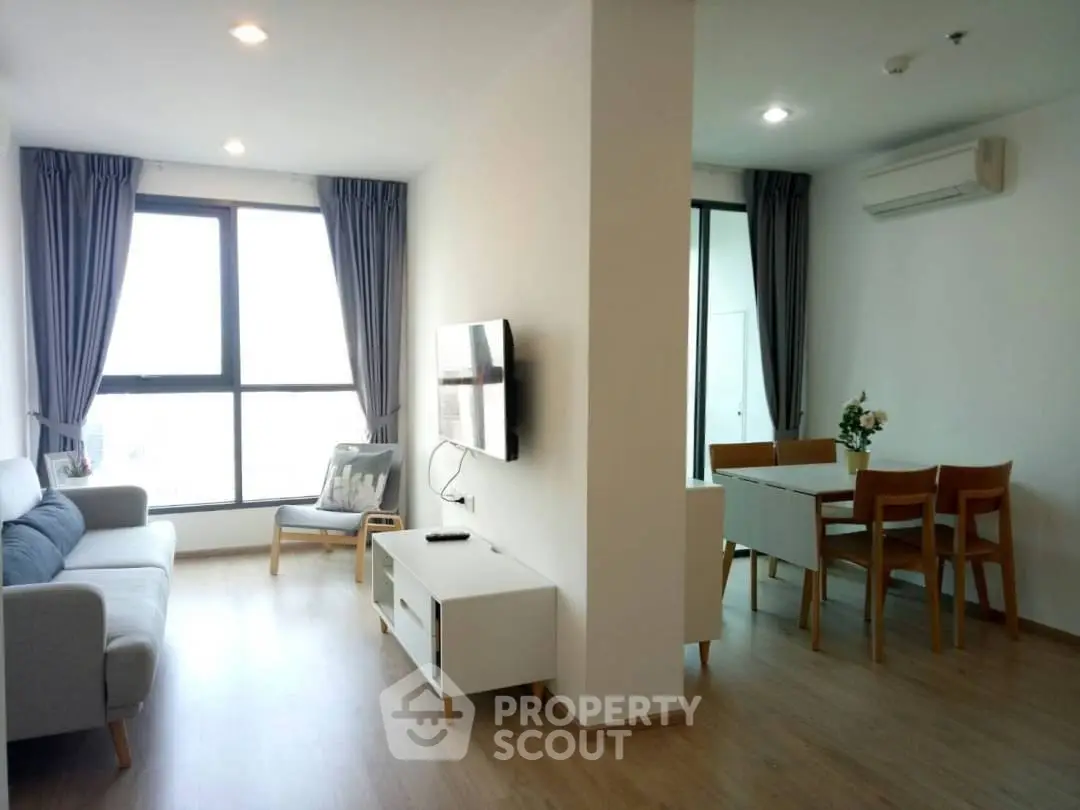 Modern living room with dining area, featuring large windows and stylish furniture.