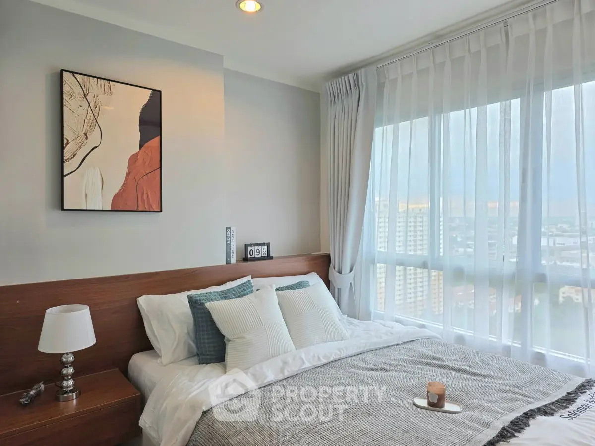 Modern bedroom with large window offering stunning city view, stylish decor, and cozy ambiance.