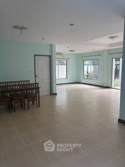 Spacious empty living room with tiled flooring and dining area, abundant natural light.