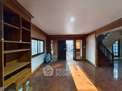 Spacious living room with wooden flooring and built-in shelves, featuring natural light and staircase access.