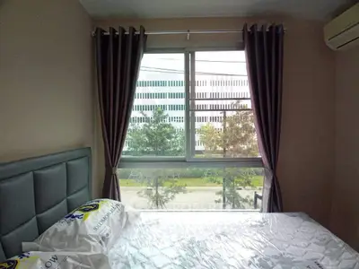 Cozy bedroom with large window offering a view of modern architecture and lush greenery.