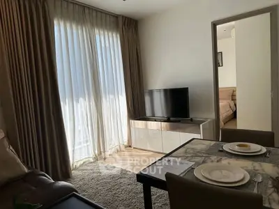 Cozy living room with TV and dining area, natural light through sheer curtains.