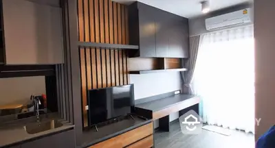 Modern studio apartment with sleek kitchenette, built-in cabinetry, and cozy living space, illuminated by natural light from the large window.