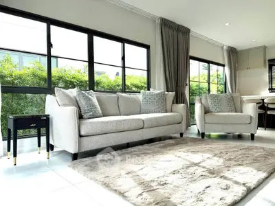 Spacious living room with modern sofa set and large windows offering lush garden views.