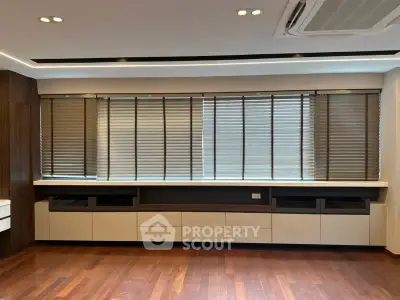 Spacious modern living room with wooden flooring and large windows with blinds.