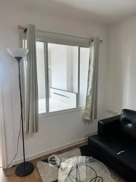 Cozy living room with modern black sofa and floor lamp, featuring a large window for natural light.