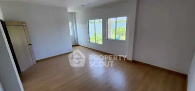 Spacious empty room with wooden flooring and large windows offering natural light.