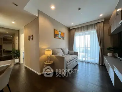 Modern living room with cozy sofa and elegant decor, featuring large window with sheer curtains.