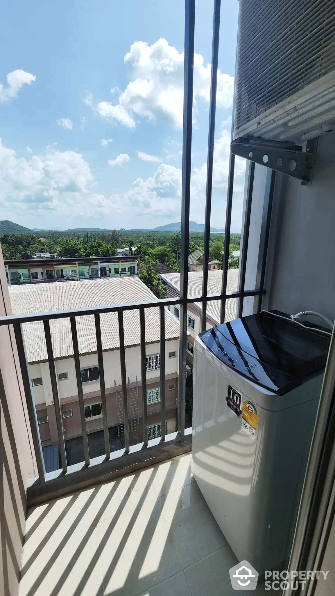 Compact balcony with a washing machine offering a serene view of the surrounding neighborhood and lush green hills, perfect for urban living.