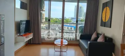 Modern living room with large windows and city view, featuring a sleek black sofa and wall-mounted TV.