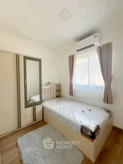 Cozy bedroom with single bed, air conditioning, and natural light through curtains.