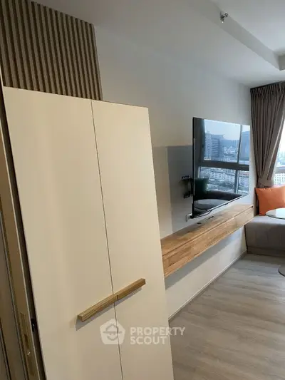 Modern living room with sleek TV setup and city view window, featuring stylish decor and cozy seating.