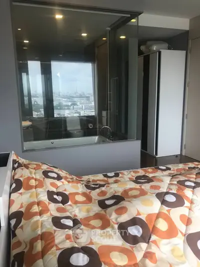 Modern bedroom with city view and glass-walled bathroom, featuring stylish decor and cozy bedding.