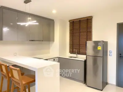 Modern kitchen with sleek cabinets, breakfast bar, and stainless steel fridge in a stylish apartment.