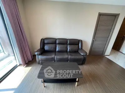Modern living room with leather sofa and wooden coffee table, featuring natural light from large window.
