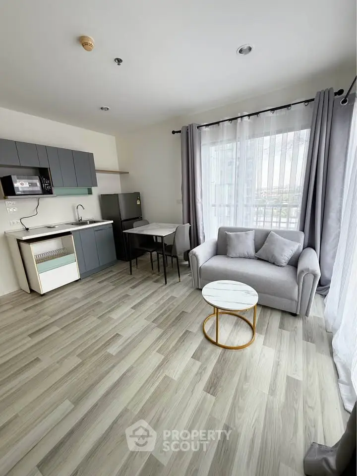Modern open-plan living room with sleek kitchen and cozy seating area, featuring large windows and stylish decor.
