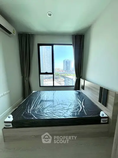 Modern bedroom with large window and city view, featuring a new bed frame and air conditioning.