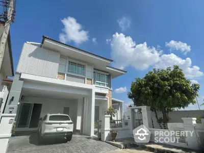 Modern two-story house with carport and lush garden under clear blue sky