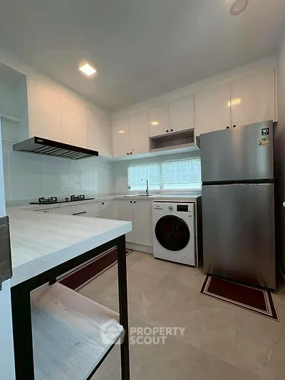 Modern kitchen with gas stove, washing machine, and stainless steel fridge