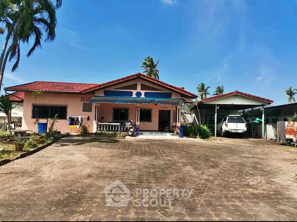 Charming single-story home with spacious driveway and carport in tropical setting.