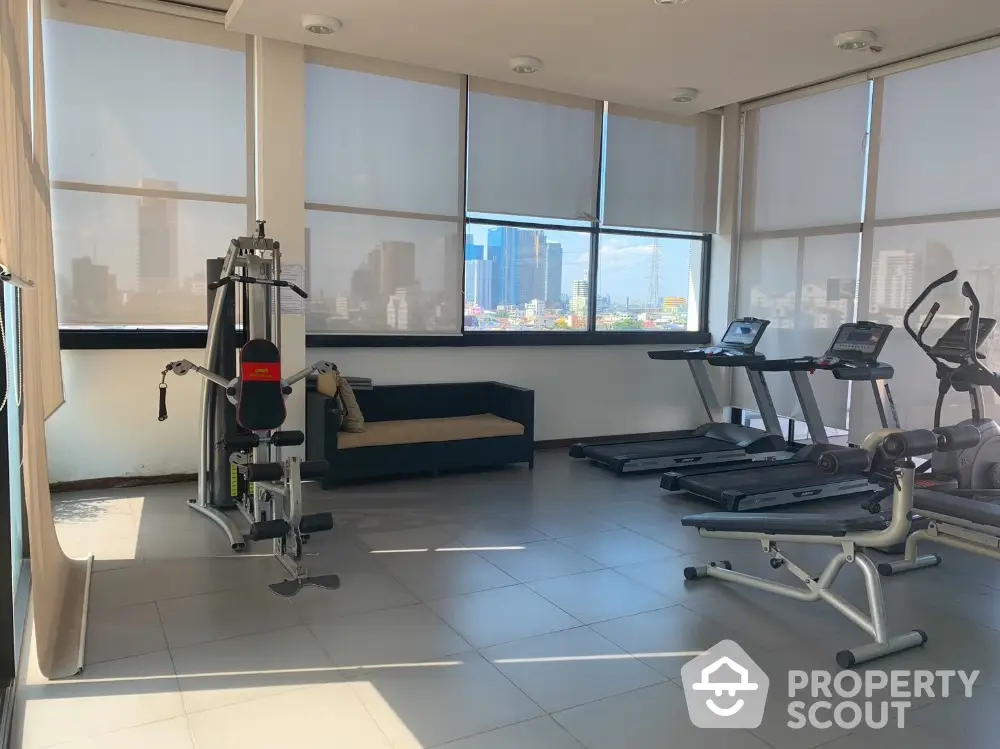 Modern gym with city view, featuring exercise equipment and natural light.