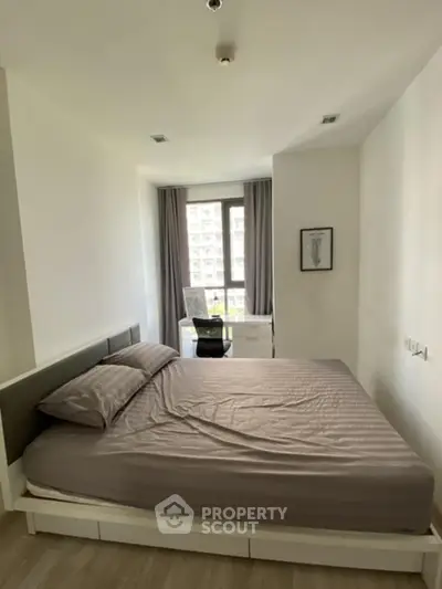 Cozy bedroom with large window and modern furnishings in urban apartment.