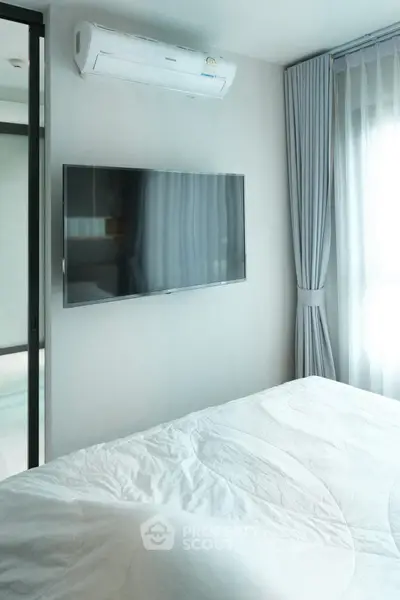 Modern bedroom with wall-mounted TV and air conditioning, featuring elegant curtains and a cozy bed.