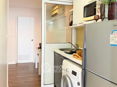 Compact kitchen with modern appliances including fridge, microwave, and washing machine in cozy apartment.
