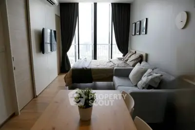 Modern studio apartment with bed, sofa, and dining area, featuring large windows and a city view.