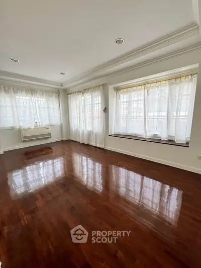 Spacious living room with polished wooden floors and large windows for natural light.