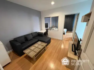 Spacious living room with gleaming hardwood floors and modern grey sofa, leading to a cozy bedroom, perfect for urban living.