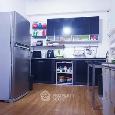 Modern kitchen with sleek black cabinets and stainless steel appliances, featuring a spacious layout and wooden flooring.