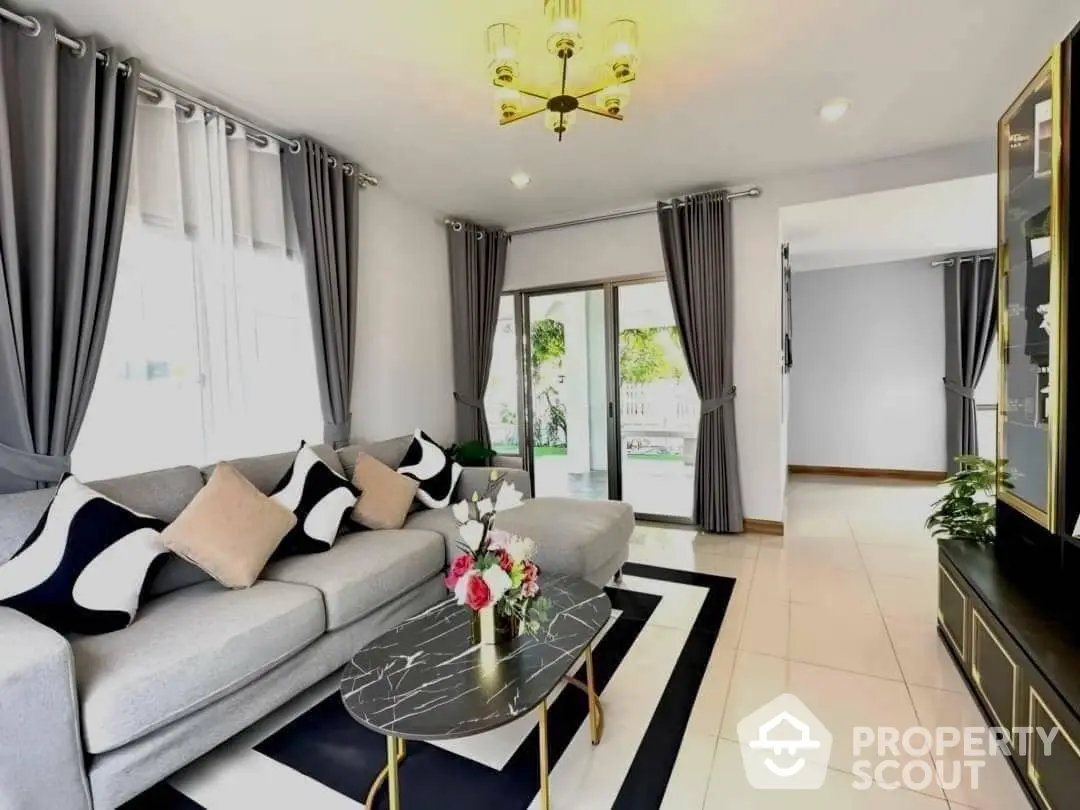 Elegant living room with plush grey sofa, chic marble coffee table, and modern decor, opening to a sunlit patio.