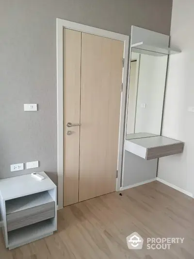 Modern minimalist bedroom with sleek wooden flooring, a large mirror, and a practical floating shelf, offering a serene and spacious atmosphere.