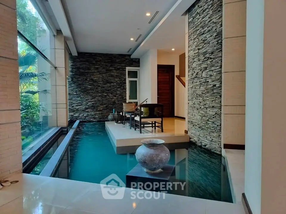 Luxurious indoor pool area with modern stone wall and elegant seating, perfect for relaxation.