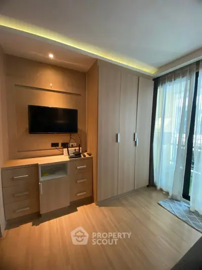 Modern bedroom with built-in wardrobe and wall-mounted TV, featuring sleek wooden flooring and natural light.