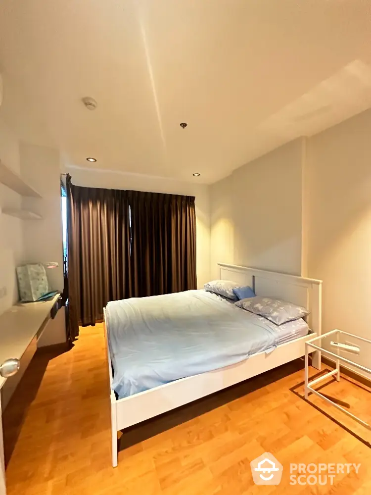 Cozy bedroom with wooden flooring and large window for natural light